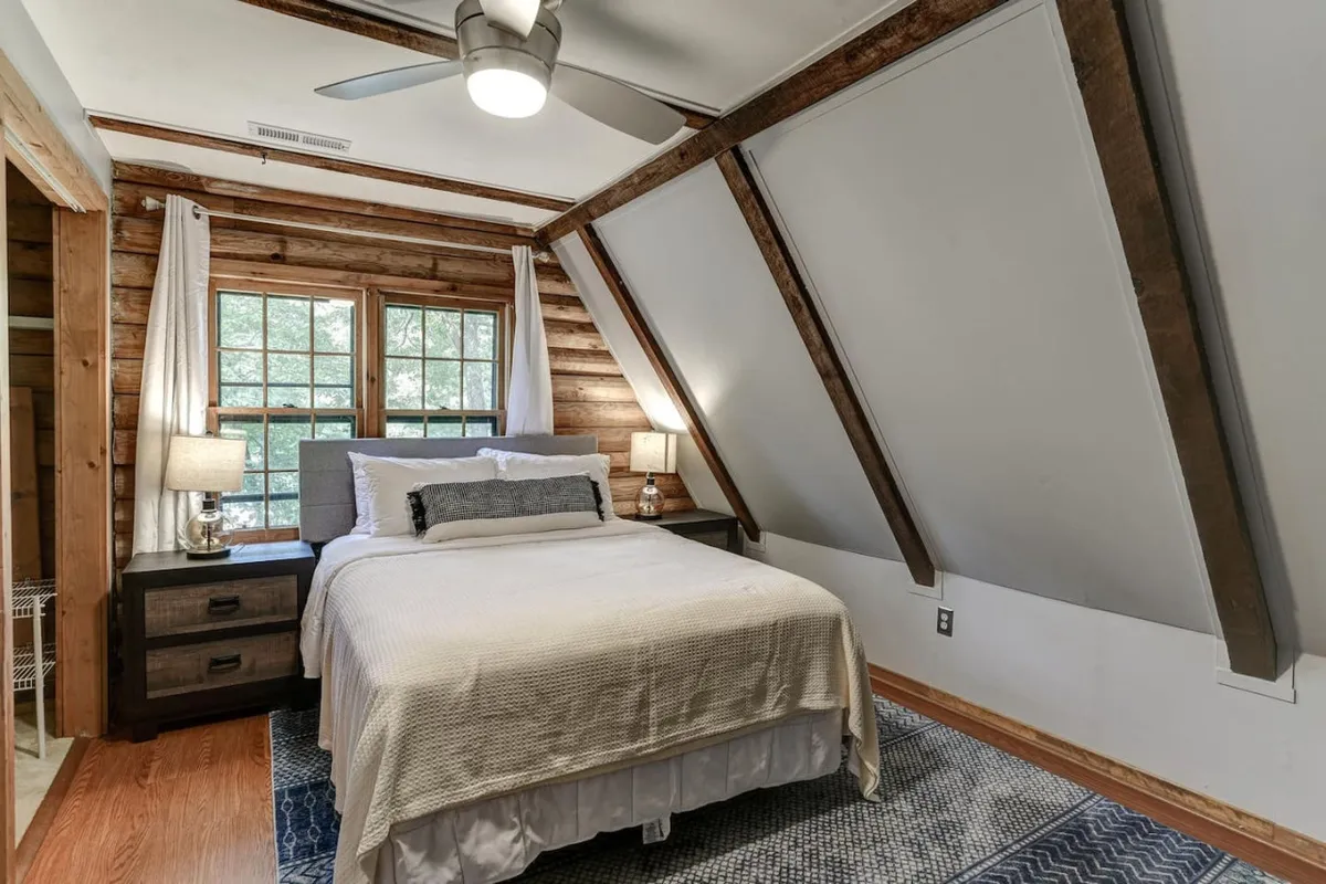 A restful bedroom with a plush bed, large windows showcasing nature views, nightstands, and soft lighting from bedside lamps. The space feels both calm and inviting, ideal for winding down or starting a quiet morning.