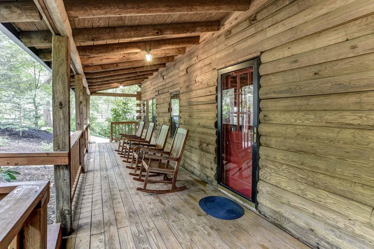 A welcoming front porch with classic rocking chairs, a red door, and views of natural surroundings. The ambiance is tranquil and inviting, suggesting a space for families to relax, share stories, and savor quiet moments together after a day of exploring.