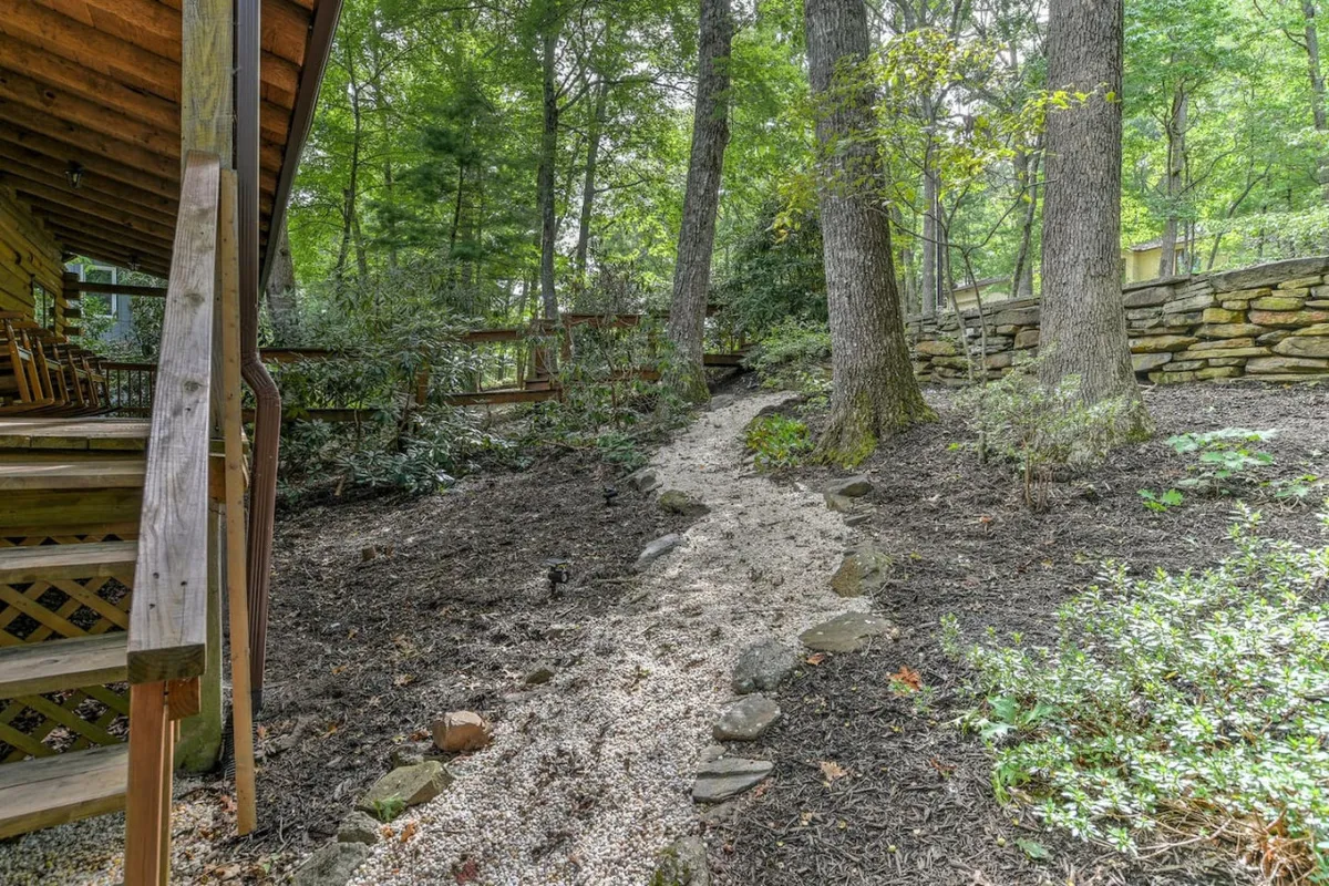 A serene path winding through lush trees leads to a cozy wooden structure. The stone wall and ample greenery suggest a private, natural retreat—an inviting spot for families to gather and enjoy quiet evenings under the stars.