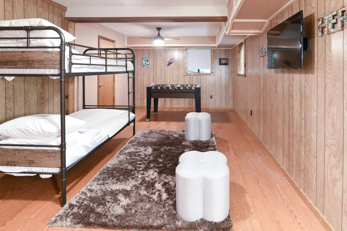 This image features a dedicated bunk room outfitted with a twin bunk bed, a foosball table, and a plush area rug. The space is styled for comfort and fun, with stools for seating and ample room for play or relaxing. The decor is inviting, casual, and distinctly kid-friendly.