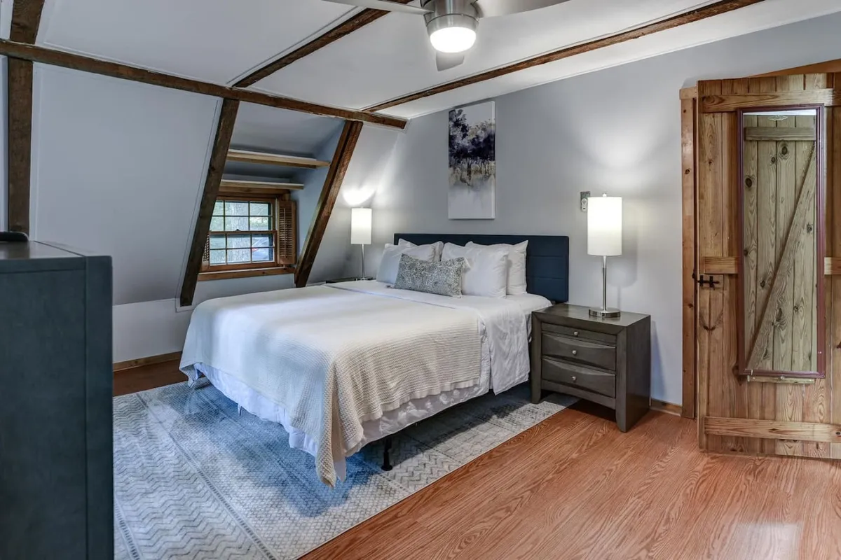 A tranquil bedroom scene with a neatly made bed, wooden door, nightstand, and wall art. Sunlight softly filters into the space, suggesting a restful environment perfect for unwinding after outdoor adventures.